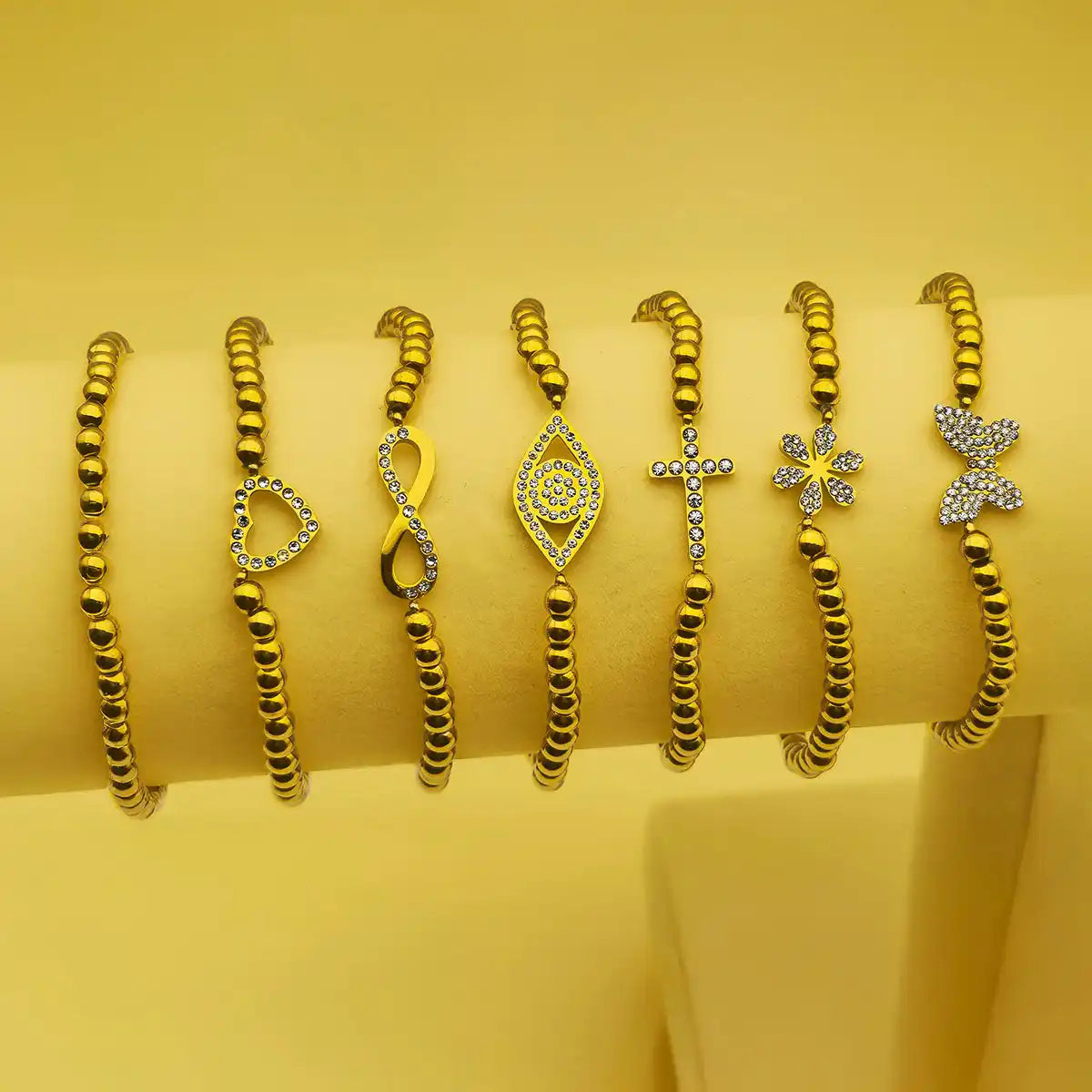 Seven gold-colored beaded bracelets with various crystal-studded charms.