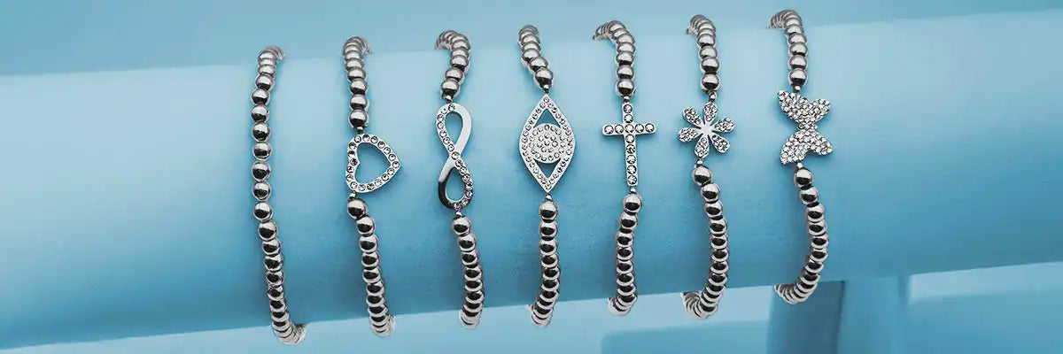 Seven silver bracelets with various charm designs.